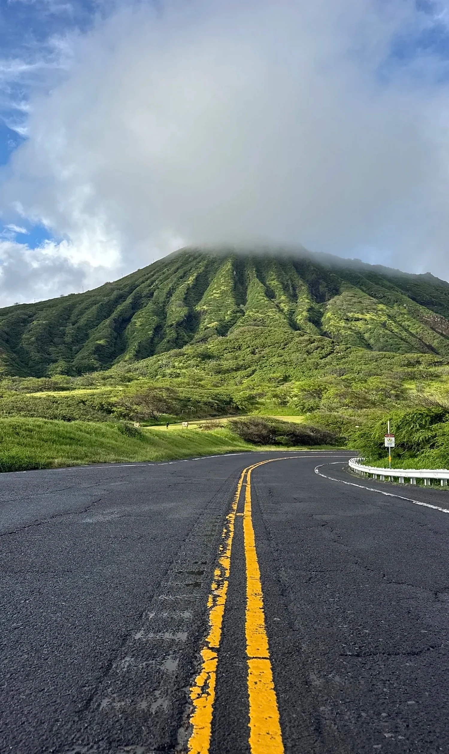 A winding O'ahu road leading toward cloud-capped mountains